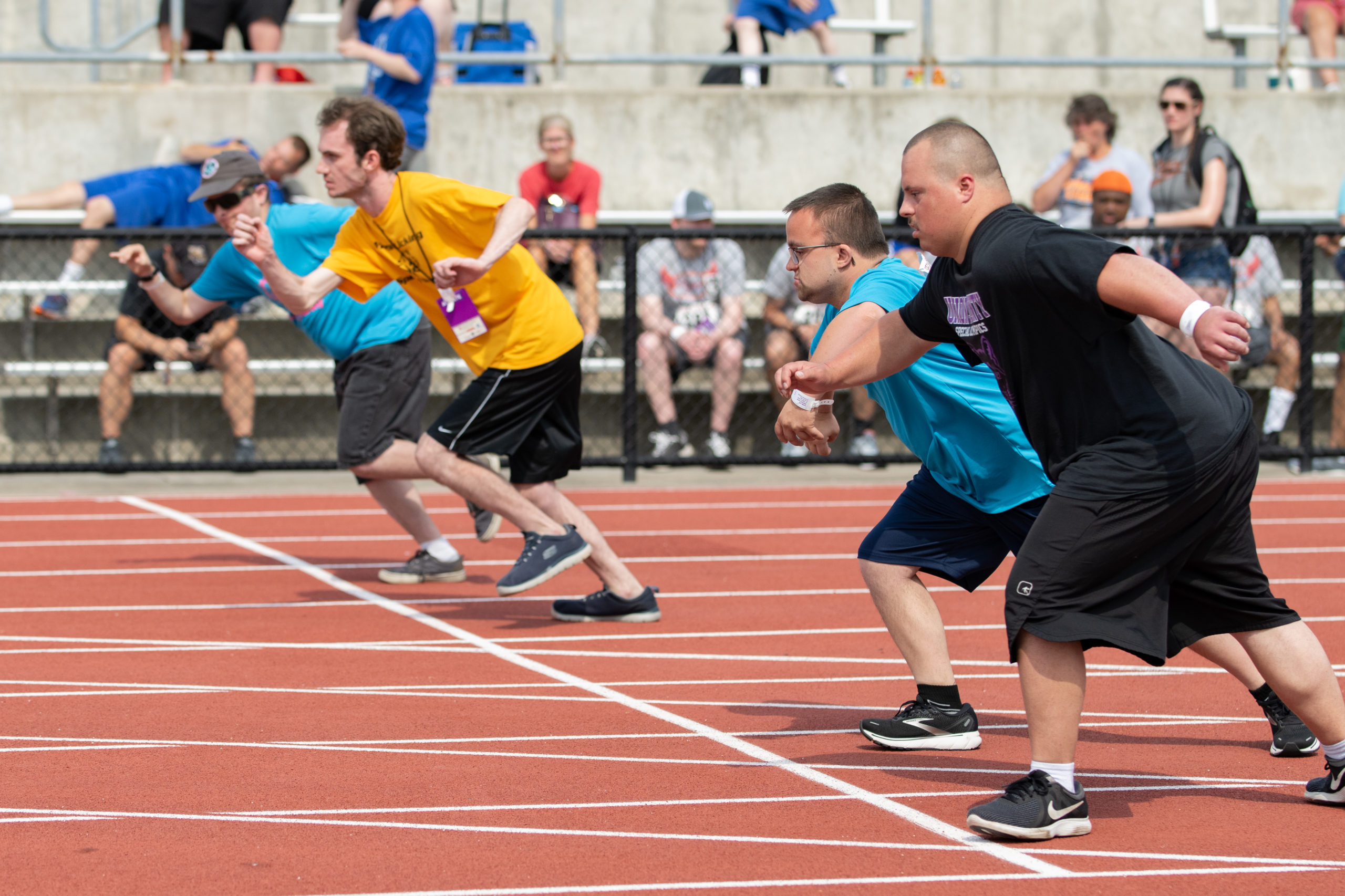 Team in green shirts march with banner on red track | state sporting events